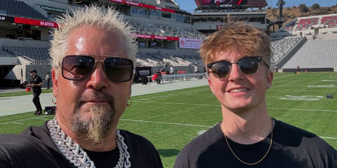 Guy Fieri, pictured left, was seen wearing black and gold David Beckham DB 7002S RHLFQ square sunglasses with grey gradient lenses at the Aztec game