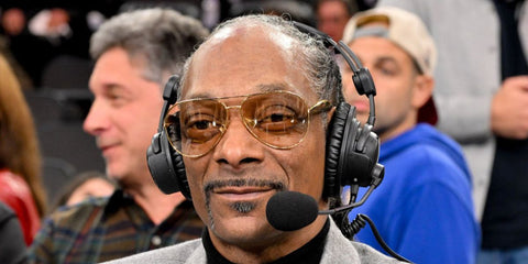 Snoop Dogg was seen wearing gold Bottega Veneta BV1305S 002 Sardine aviator sunglasses with light brown lenses during a basketball game between the Los Angeles Clippers and the Golden State Warriors, January 2026.